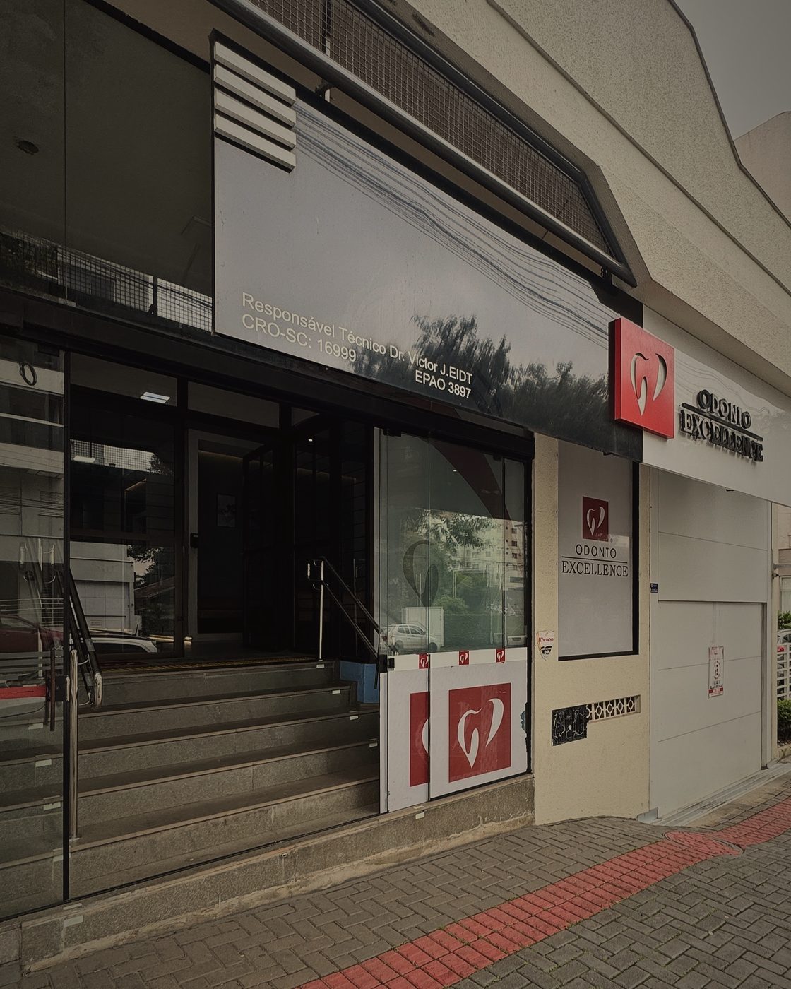 Entrada da Odonto Excellence na Rua Clevelândia, com a escada, as portas de vidro e o logo da clínica