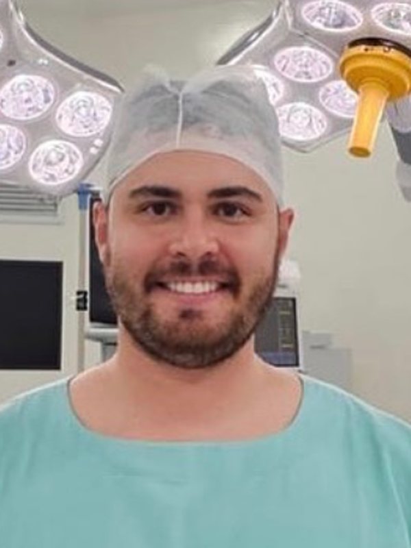 Dr. Davi Cadore, de touca e roupa cirúrgica, sorrindo no centro cirúrgico