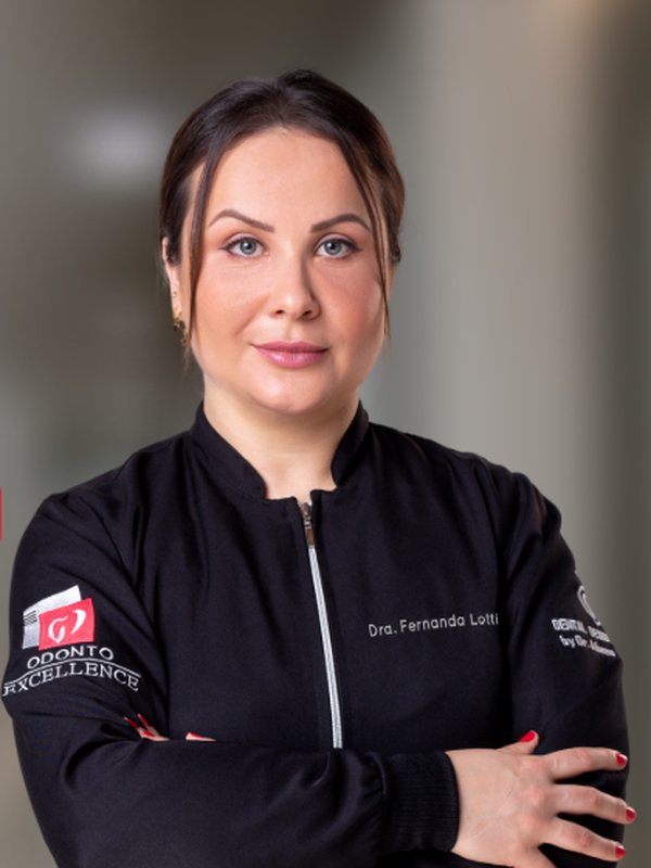 Dra. Fernanda Lotti, de jaleco preto, de braços cruzados