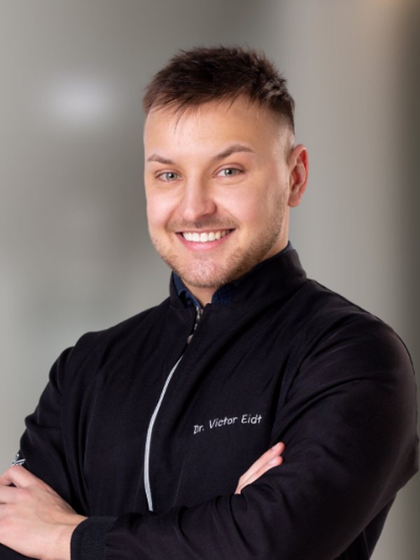 Dr. Victor J. Eidt, de jaleco preto, sorrindo de braços cruzados